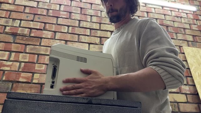 Man holding old printer near wall, handling equipment and preparing for installation or placement indoors