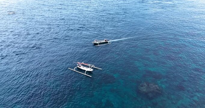 Drone aerial footage of traditional Balinese outrigger boats floating above clear blue waters and coral reef formations near the coast of Amed, Bali, Indonesia.