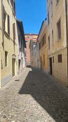 Fototapeta premium Narrow cobblestone alley in a historic Italian village, sunlight creating dynamic shadows on old building facades