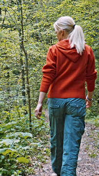 A caucasian woman explores a lush forest trail, embodying the serenity of nature during springtime. Her casual attire complements the greenery around her as she hikes on a serene path.