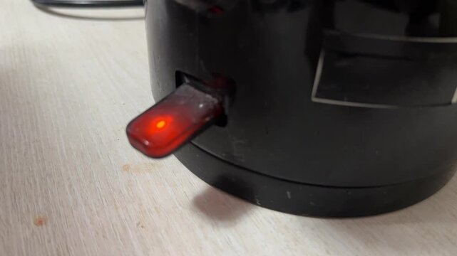 electric kettle power button with glowing red indicator light, kitchen appliance switch close up