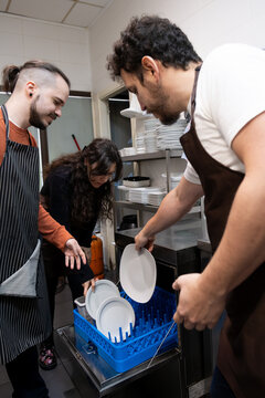 Restaurant staff loading dirty dishes into commercial dishwasher for cleaning