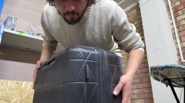 Man rolling suitcase to check wheels, travel preparation and luggage testing concept, verifying mobility and functionality of bag in indoor environment