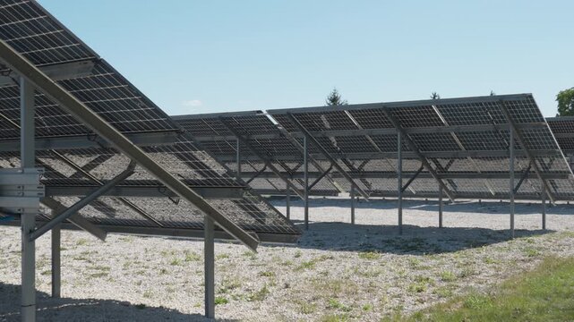 Bifacial solar panel array at farm with white gravel for sunlight reflection. Rear view of photovoltaic modules on ground mounting structures for renewable electricity production system.