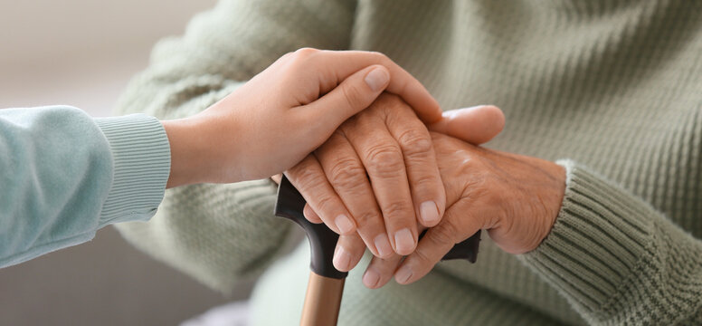 Woman holding grandmother's hands with stick at home, closeup