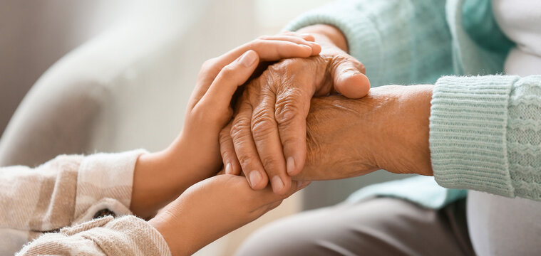 Senior woman with daughter holding hands at home, closeup