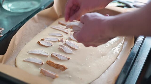 In a kitchen, a person is preparing a layered dish by adding various toppings onto the batter.