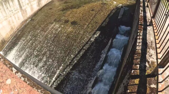 Rushing water flowing over a concrete weir in an artificial canal, creating energy and turbulence