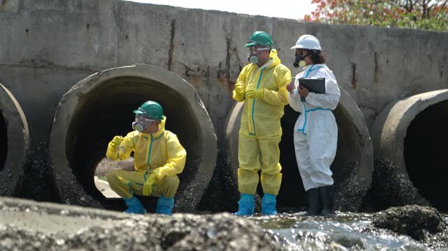 Environmental response team in hazmat suits collecting wastewater samples near industrial sewage drainage pipes
