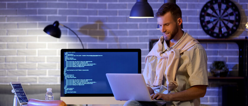 Young bearded programmer working with laptop in office at night