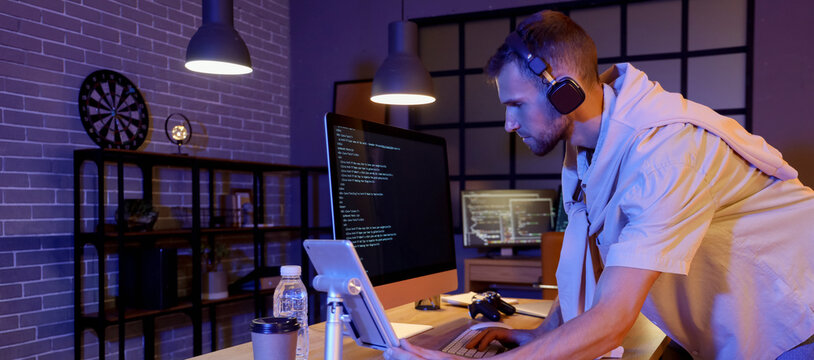 Young bearded programmer with headphones working in office at night