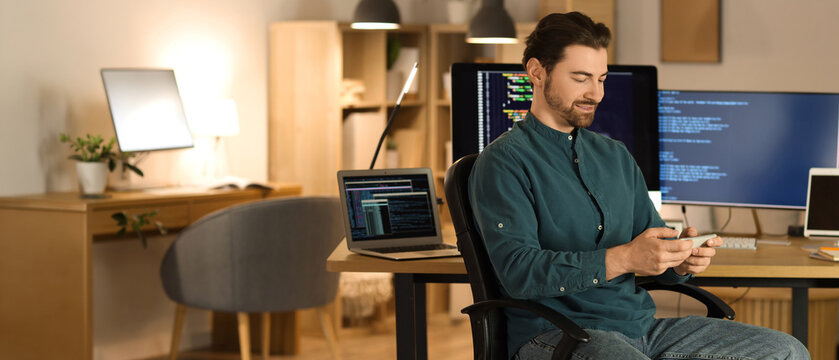 Male programmer with phone at workplace in office