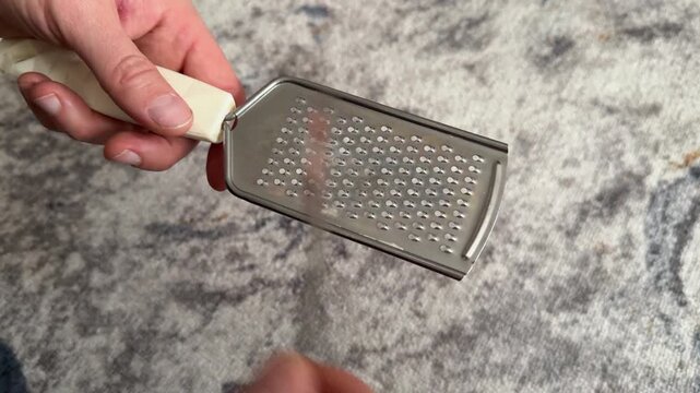 Person tapping metal grater with fork close up at home, producing rhythmic sound, improvised percussion activity, creative hobby concept