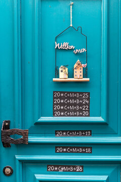 View of a bright turquoise wooden door featuring a decorative welcome sign and traditional chalk inscriptions in Monreal, Rhineland-Palatinate, Germany.
