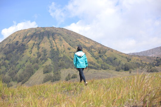 Female traveler walking through green savanna with the majestic Mount Batok Bromo as a backdrop.