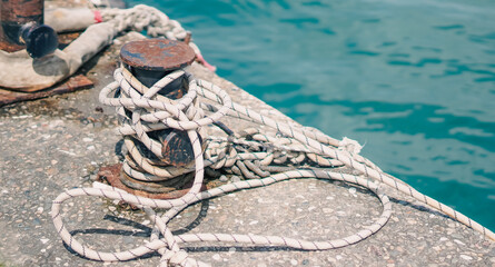 Fototapeta premium A rusty metal bollard with white mooring ropes on a concrete pier by the sea.