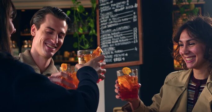Slow Motion Of Friends Toasting Cocktails During Social Gathering In Modern Caf&eacute;. Young adults raising colorful cocktails for a cheerful toast inside a contemporary caf&eacute; or lounge.
