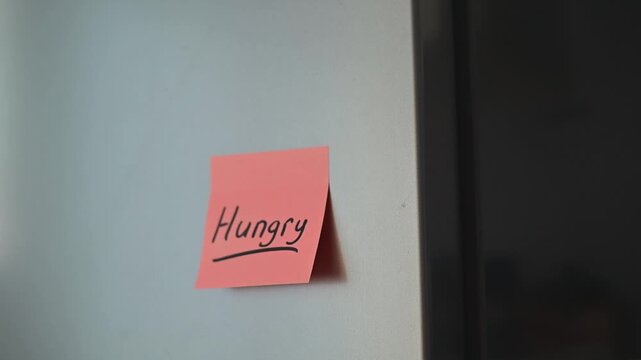 A hand reaches for a door handle before placing a note labeled hungry on a wall. This action may indicate a desire for food or a reminder to eat, highlighting a moment of thought and intention
