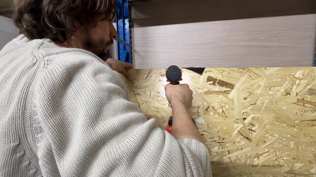 Man driving screw into wooden board using power screwdriver, construction and assembly concept, fastening material with electric tool