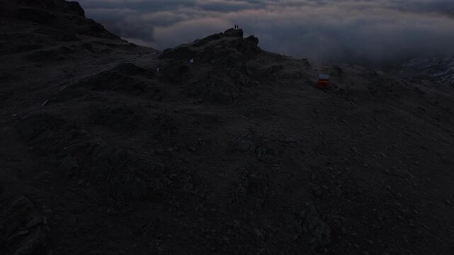 Aerial flyover over hikers enjoying the sunrise glow over the inversion of clouds in the Swiss Alps with a pan up panoramic view of the mountains and colorful sky at dawn