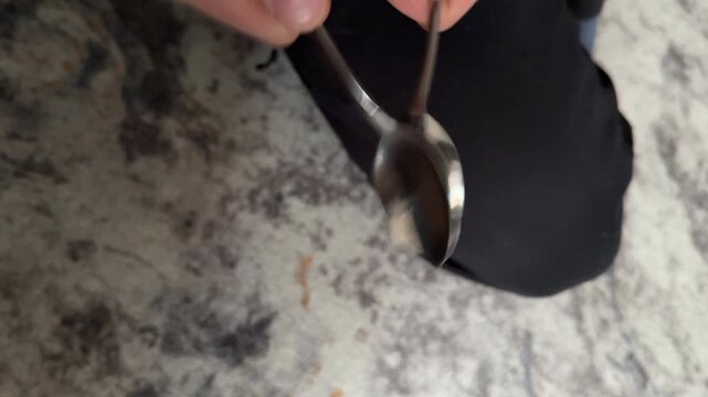 Person tapping spoon against another spoon close up at home, producing metallic sound, simple sound experiment, everyday object interaction, creative curiosity concept