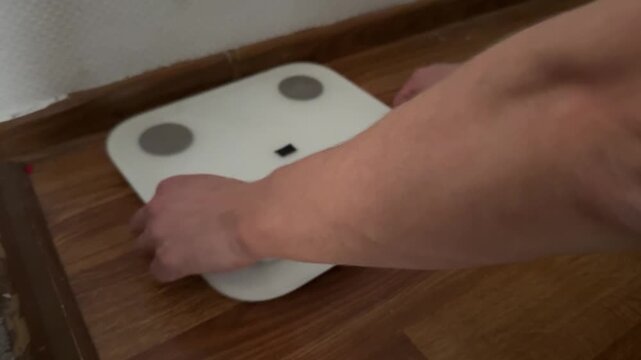 man moving digital scale on floor at home, adjusting position, household object placement, daily routine, real people