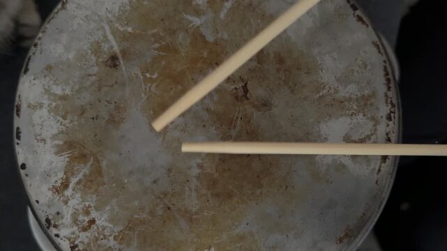 Person hitting metal pot with wooden sticks close up, creating rhythm like drum, improvised percussion activity, creative hobby concept
