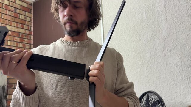 Man assembling monitor stand parts, connecting mounting components, equipment setup and workstation preparation indoors