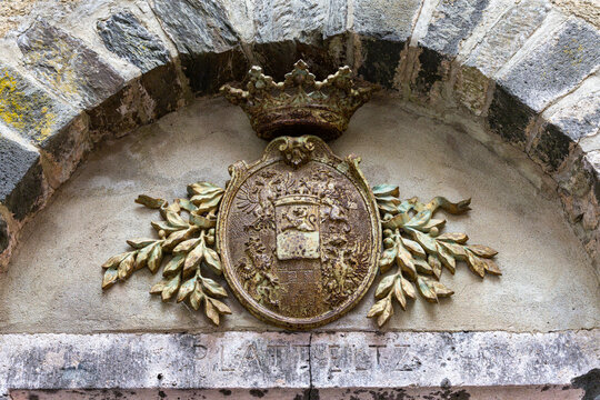 View of the historic coat of arms of Eltz Castle featuring a weathered heraldic shield with a crown and leafy branches under a stone archway in Wierschem, Rhineland-Palatinate, Germany.