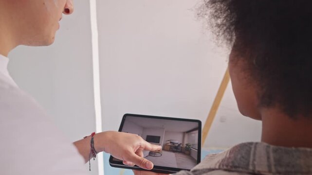 A young couple collaborates on a tablet in their renovated living room. They discuss layout changes, blending technology and home improvement.