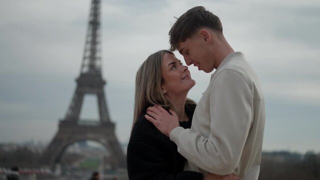 A young couple embraces affectionately in Paris France with the Eiffel Tower visible in the background The soft overcast light creates a romantic atmosphere as the lovers share an intimate moment in f