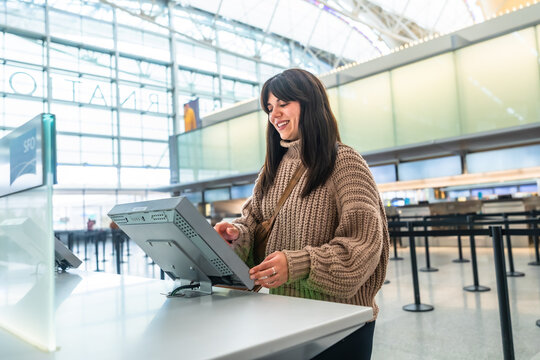 Woman using self service check in kiosk at airport terminal