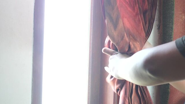 A man tying back a green curtain to allow morning sunlight into a dark room.