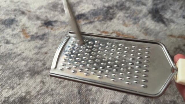 Person tapping metal grater with fork close up at home, producing rhythmic sound, improvised percussion activity, creative hobby concept