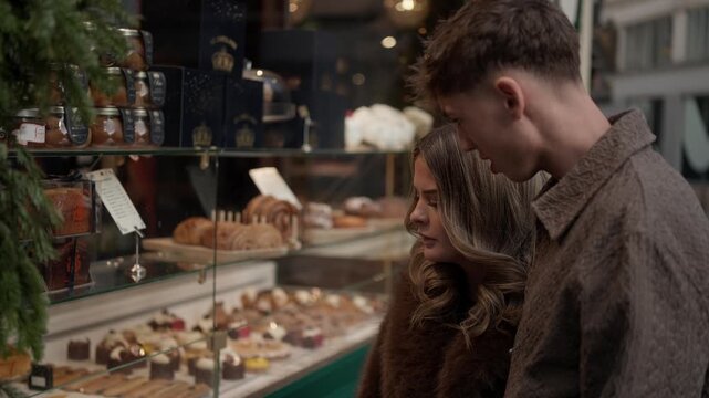 A young couple in Paris France are window shopping at a patisserie They are looking at the cakes and pastries displayed in the shop window The scene captures a romantic outing in the city.