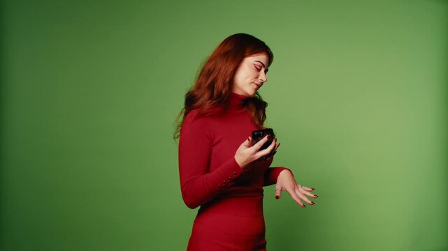 Happy young woman in red clothes listening to music on her smartphone against a green screen background.
