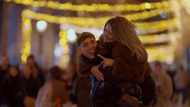 A young couple enjoys a piggyback ride through the streets of Paris at night The happy man carries his girlfriend on his back as they navigate a crowded street illuminated by festive bokeh lights cele