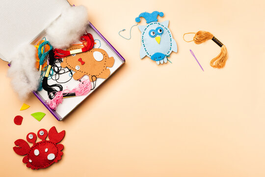 Kids felt sewing craft kit with colorful DIY toy materials, embroidery threads, stuffing, needle, and unfinished handmade animal ornaments on pastel background with copy space. Creative hobby activity