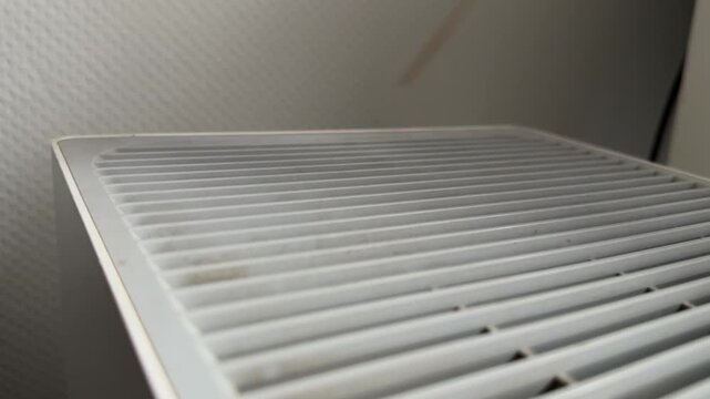 Person sliding wooden stick along air purifier grille close up at home, producing vibrating sound, improvised interaction, everyday object experiment concept