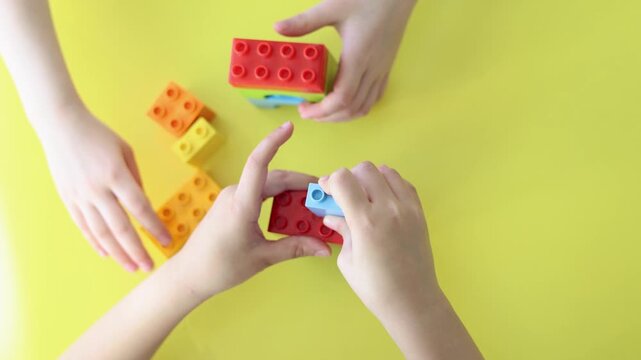 Close-up of two kids' hands as they play with a construction set, carefully assembling colorful pieces. Their teamwork and creativity shine as they build imaginative structures together.