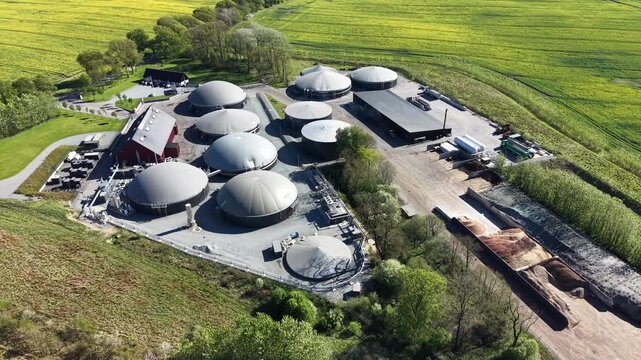 Vertical aerial perspective of biogas tanks, storage sheds, and organic matter piles at a renewable energy site in Denmark.