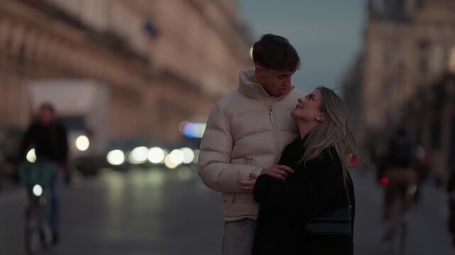A young couple is embracing on a city street in Paris France at dusk The background features blurred traffic and soft lighting creating a romantic atmosphere.