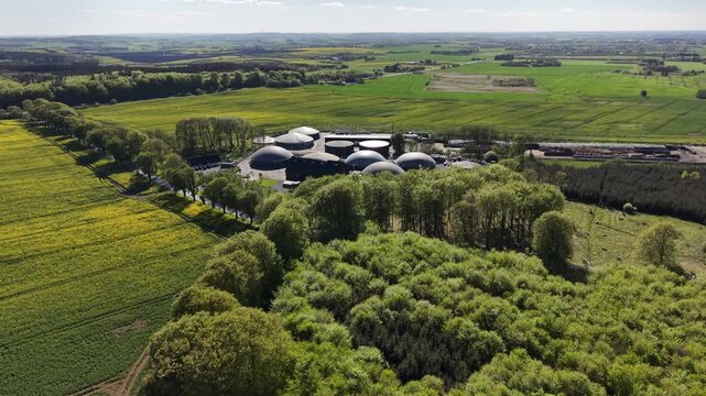 High angle view of a bio-methane plant situated between a lush green forest and bright yellow rapeseed fields in rural Hammel.