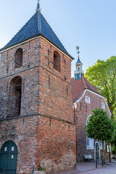 View of the historic Greetsieler Kirche brick church and its separate bell tower under a clear blue sky in Krummhorn, Lower Saxony, Germany.