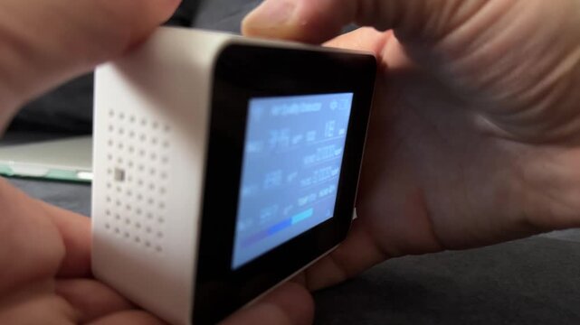Person turning on air quality monitor device close up at home, activating sensor, measuring indoor air conditions, technology use concept