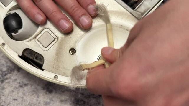 Hands installing brush attachment on robot vacuum cleaner underside, smart home appliance maintenance and setup concept