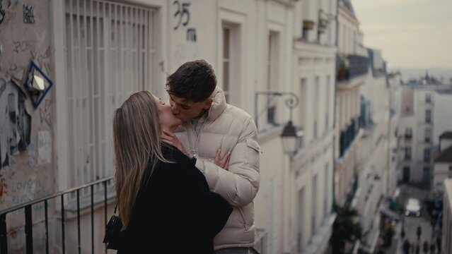 A young couple kisses romantically on a street in Montmartre Paris France The image showcases love and affection in an urban setting with old buildings and graffiti suitable for travel and lifestyle c