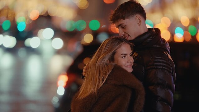 A romantic couple embraces in Paris France at night with a bokeh lights background The young man and woman are in love creating a warm and affectionate urban scene with city lights.
