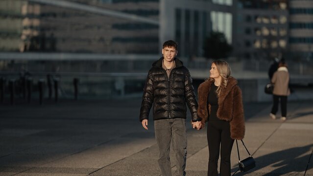 A romantic couple is holding hands and walking together in Paris France with modern architecture in the background They are wearing winter fashion and enjoying a moment of love and affection in the ci