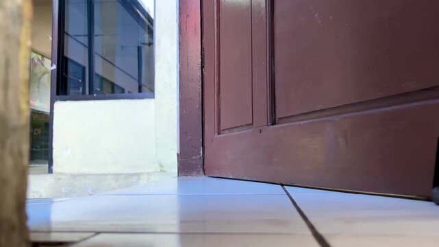 An Asian man is trying to open the door to enter the room by opening the door with the condition that the bottom of the door has a support wheel or door retaining wheel.